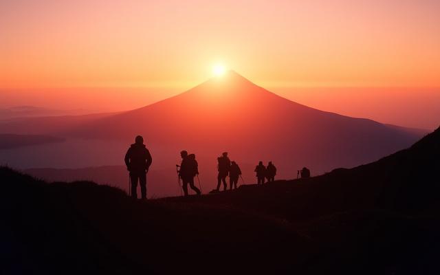 A small group of hikers silhouetted against the rising sun, viewing Mount Fuji from a pristine trail with clear skies, capturing the essence of a challenging yet rewarding expedition.